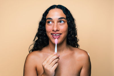 Portrait of young woman applying make-up against pink background