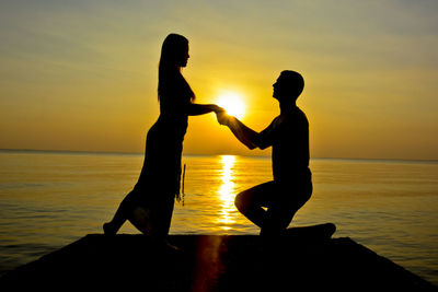 Silhouette of couple standing against sea during sunset