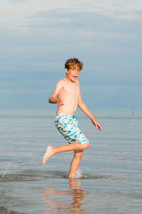 Full length of shirtless boy in sea against sky