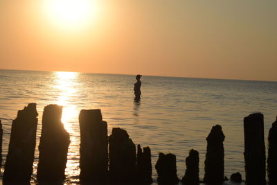 Silhouette person on sea against sky during sunset