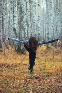 Full length of woman with arms outstretched bending in forest
