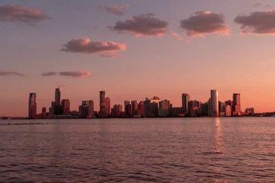 Sea by buildings against sky during sunset