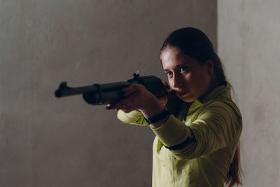 Woman aiming gun against wall