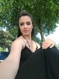 Portrait of a beautiful young woman standing against trees