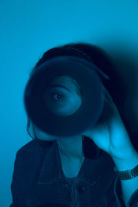Portrait of woman against looking through circle against blue background