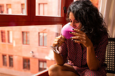 Ethnic thoughtful latin woman enjoying a healthy kefir and pitaya smoothie sitting by the windows at home