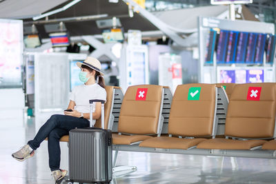 Woman wearing mask with luggage sitting in airport