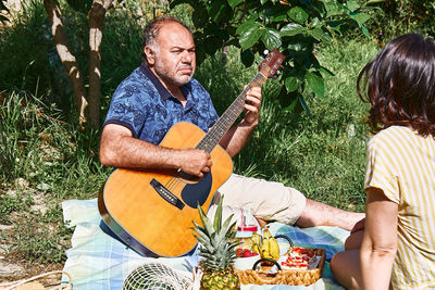 Middle aged couple having a picnic in the garden with fresh exotic fruit and sweet sandwiches.