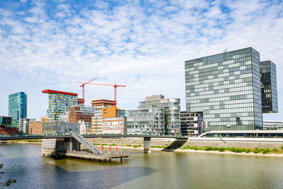 Buildings by river against sky in city
