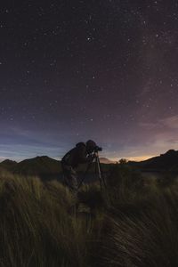 Side view of man photographing while standing on field against sky at night