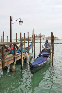 Traditional gondola moored by wooden post in sea against sky