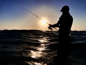 Silhouette man fishing at sea against sky during sunset