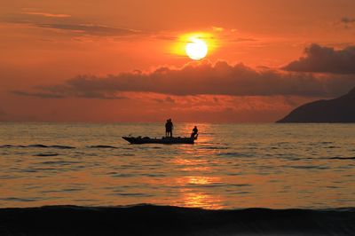 Silhouette people in sea against sky during sunset