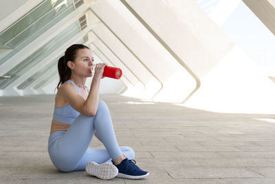 Fit, sporty woman sitting drinking water from a glass bottle after exercise or running. 