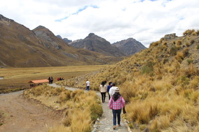 Rear view of people walking on mountain road against sky