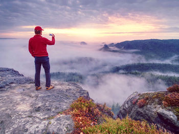 Male traveler using phone sharing fall mountains landscape view for friend through scial network