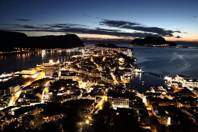 High angle view of illuminated city by sea against sky