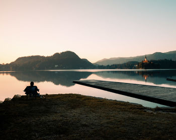 Scenic view of lake with man on chair against clear sky