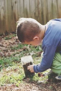 Boy looking at dirt in container on grass