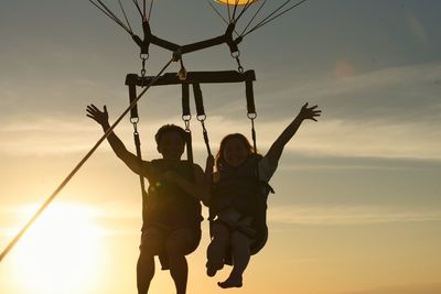 Couple in parasailing against sky during sunset