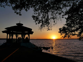 Silhouette built structure by sea against sky during sunset