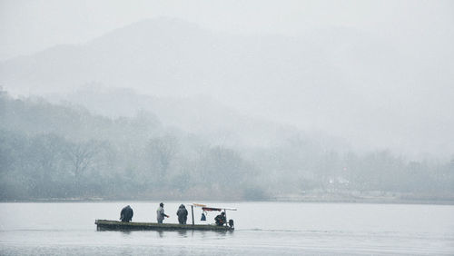 People in snow on lake against sky during foggy weather