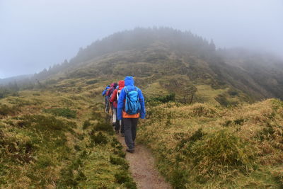 Rear view of people hiking on mountain during foggy weather