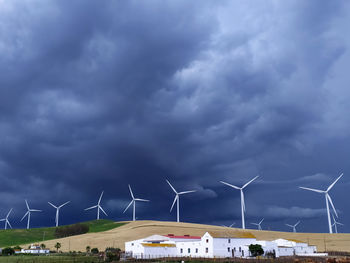 Windmills on landscape against cloudy sky