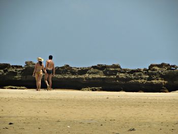 Rear view of friends standing on sand at beach