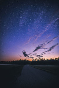 Road amidst land against star field at night