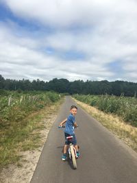 Portrait of boy cycling on road amidst field against sky