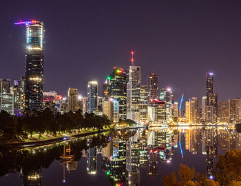 Illuminated modern buildings in city against sky at night