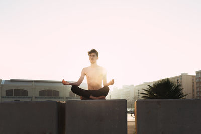 Full length of shirtless man sitting against clear sky