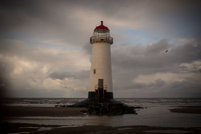 Lighthouse by sea against sky during sunset