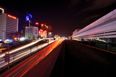 Light trails on road amidst illuminated buildings in city at night