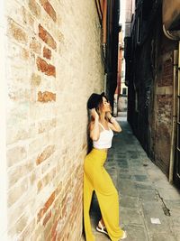 Side view of young woman standing by brick wall in alley