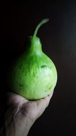 Close-up of hand holding apple against black background