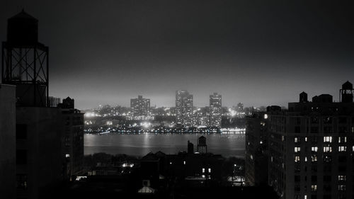 Illuminated cityscape by sea against clear sky at night