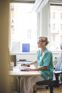 Side view of mature doctor working over computer while sitting in clinic