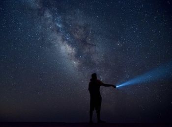 Rear view of man with arms raised standing against sky at night