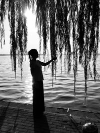 Silhouette woman standing on footpath by lake at sunset