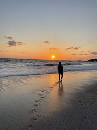 Silhouette woman standing on beach against sky during sunset