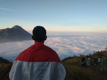 Rear view of man standing on mountain against sky during sunset