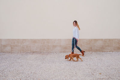 Full length of woman with dog walking on footpath against wall