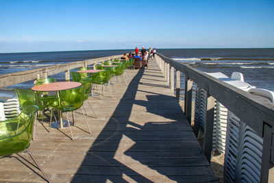 People on pier over sea against blue sky