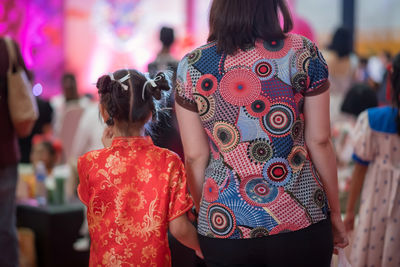 Rear of mom hold hand of girl with red china satin qipao cheongsam dress to celebrate 2024 new year