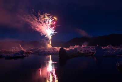 Firework display over sea against sky at night