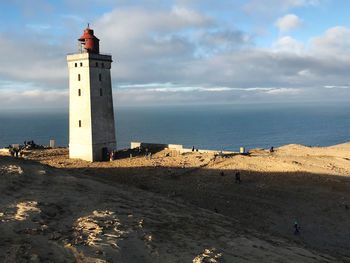 Lighthouse on beach by sea against sky