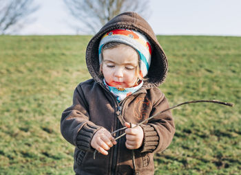 Cute girl holding stick while standing on grassy field against sky