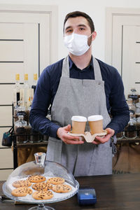 Barista serving coffee in takeaway cups in coffee shop in protective mask. coffee to go during